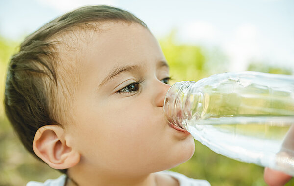 Kleinkind trinkt Wasser aus einer Flasche.