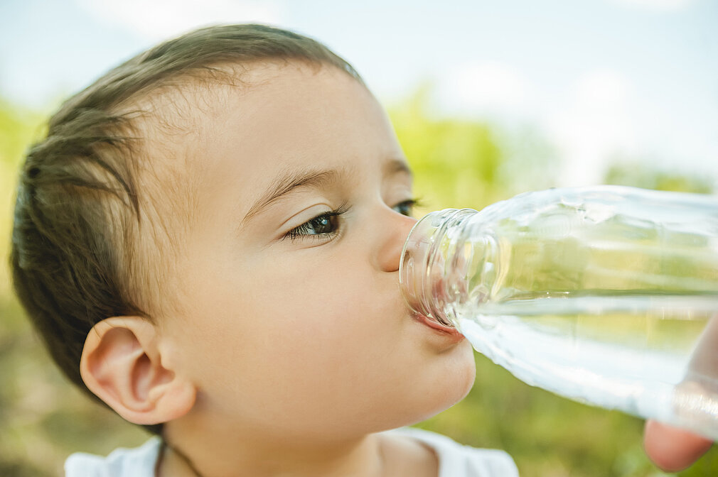 Kleinkind trinkt Wasser aus einer Flasche.