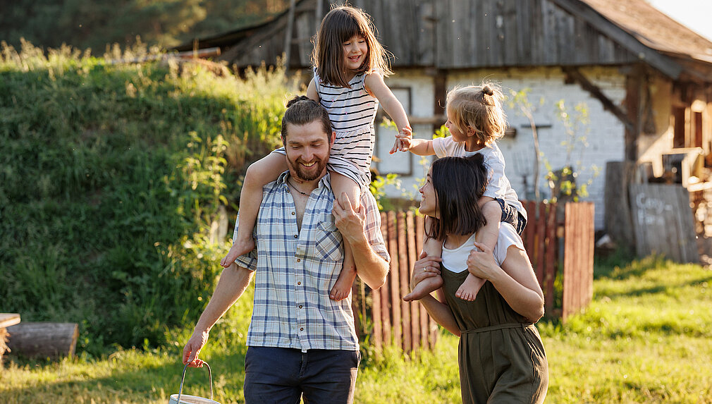 Glückliche Familie im Grünen. Eltern tragen Kinder auf ihren Schultern.