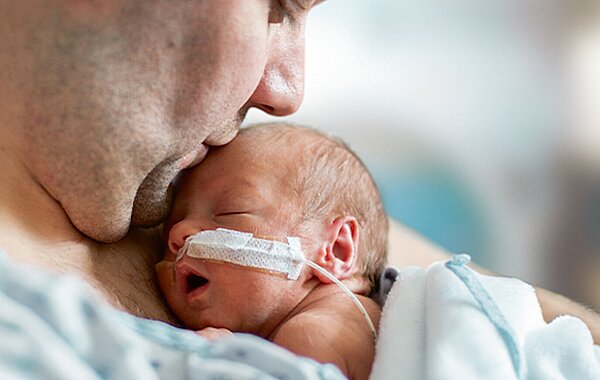 Frühgeborenes Baby, Frühchen, liegt beim Vater auf der Brust. Es hat einen Schlauch in der Nase.