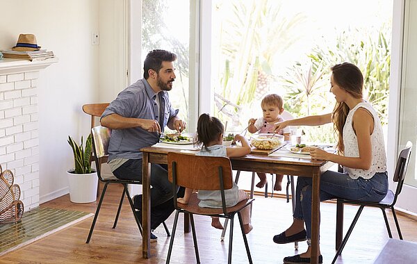 Mutter Vater und zwei Kinder sitzen am Tisch und essen.