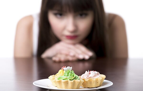 Teenager Mädchen sitzt vor Cup cakes und sieht sie nur an.