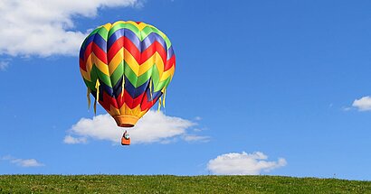 Bunter Heißluftballon schwebt auf eine grüne Wiese zu.