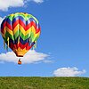 Bunter Heißluftballon schwebt auf eine grüne Wiese zu.