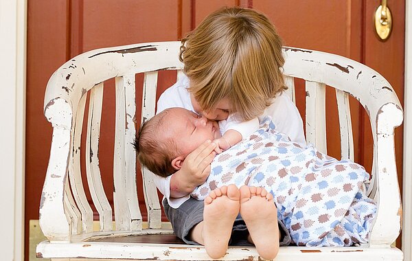 Geschwister auf Bank. Größeres Kind küsst Baby.