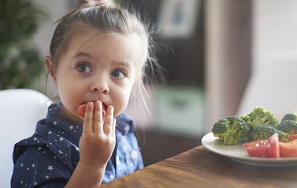 Kleines Mädchen isst Gemüse mit der Hand