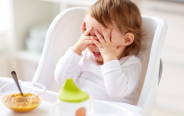 Kleinkind sitzt im Hochstuhl und möchte nicht Essen. Hält Hände vors Gesicht.