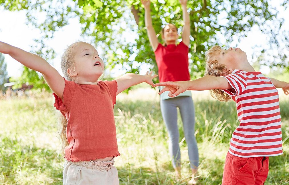 Kinder strecken sich draußen im Grünen fröhlich zur Entspannung in die Luft.