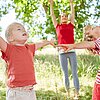 Kinder strecken sich draußen im Grünen fröhlich zur Entspannung in die Luft.