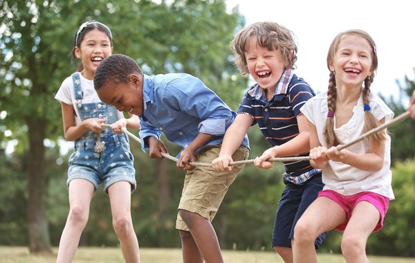 Vier Kinder ziehen lachend am Tau und spielen Tauziehen auf der Wiese.